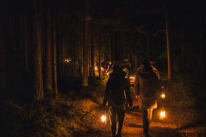 Walkers carrying lanterns along a dark wooded path